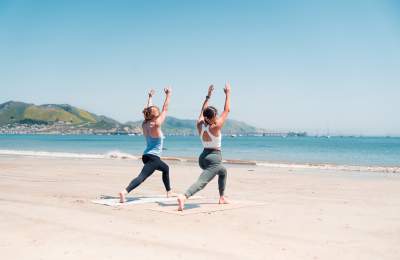 Two women doing yoga on the beach looking at the ocean