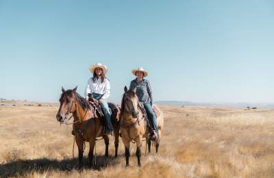 Two women on horseback with cowboy hats on Camatta Ranch among golden grass