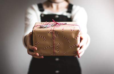 Person in soft focus holding out a wrapped present to the camera
