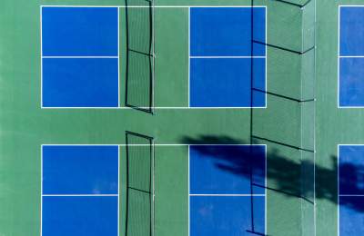 Green and blue pickleball courts shown from a birds eye view with 2 in frame and 2 more courts off to the side