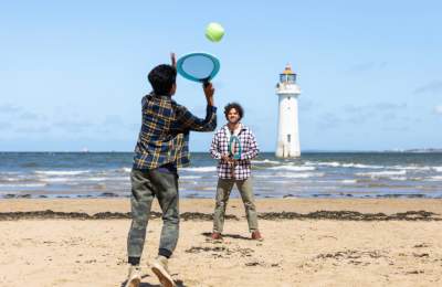 A father and son play tennis on New Brighton beach with New Brighton lighthouse in the background