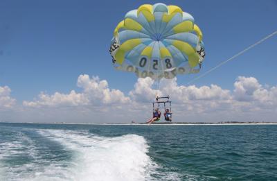 Guests flying high over clear emerald waters during a Destin parasail tour