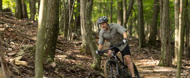 A man rides a bike on a rough mountain trail through the woods.