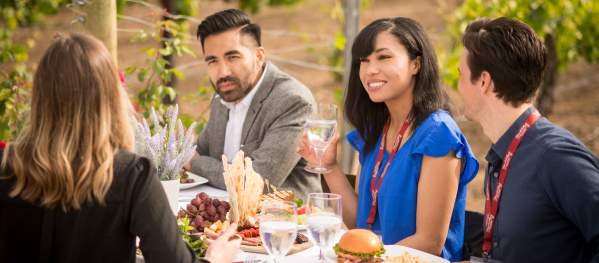 A group of friends enjoys a meal at a vineyard, outdoors