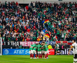 A huddle of soccer players in front of a goal in a crowd-filled stadium