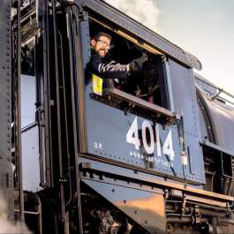 Engineer waving from the cab of the world's biggest train engine, Union Pacific 4014, with steam rising around it.