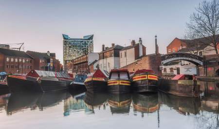 Canal boats moored at Gas Street Basin Birmingham in front of bring building a a large cubed glass building behind