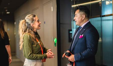 A woman with blonde hair and green jacket talks to a potential investor dressed in a business suit and pink pocket square at a WMG event.
