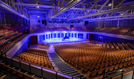 A large event venue with modern wooden effect seating and large lit stage with piano