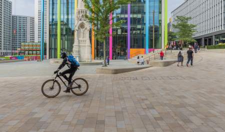 A cyclist crosses in front of the fountain in Paradise, Birmingham, with city dressing for the 2022 Commonwealth Games in the background