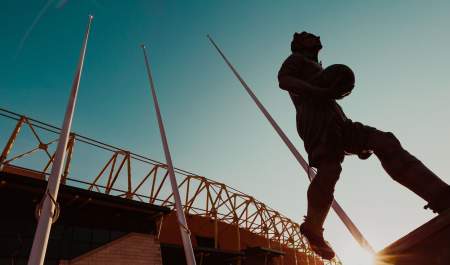 Statue of Billy Wright outside Molineux Stadium, silhouetted against the sky as the sun sets