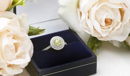 A stunning engagement ring in a box surrounded by pale pink roses