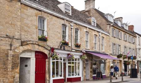 A couple walking past shops with pretty frontages and hanging baskets in Chipping Norton town centre