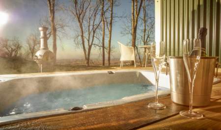 Hot tub bath at the Hilly Huts on FArncombe Estate. Steam rising from tub with bottle of sparkling wine, glasses and chimnea in background