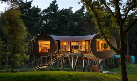 A u-shaped treehouse on stilts surrounded by trees