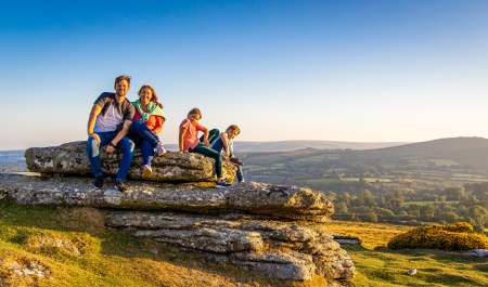 a family of two adults and two children sitting on a flat rock in Dartmoor with spectacular view behind them