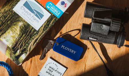 An overhead shot of the table, including an OS map, pair of black binoculars, Plovery room tag and key, and Church Farm/ Walking the Wolds business cards.