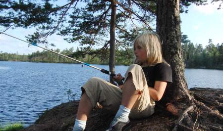 En gutt som sitter lent inntil ett tre og fisker