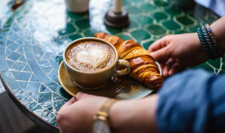 Kaffekopp med hjerteskum og en croissant servert på ett bord