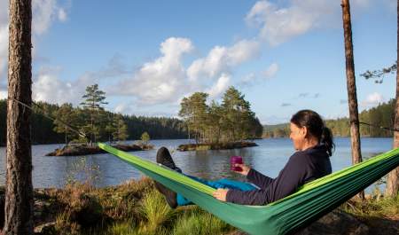 En dame som ligger i en hengekøye og speider utover vannet og flott natur