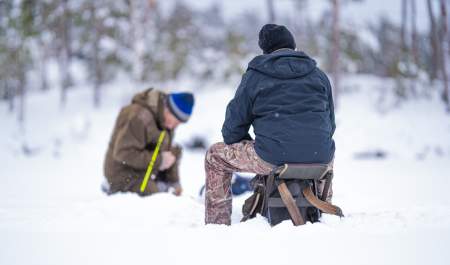 Two people sitting on the ice and ice fishing
