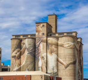 a mural painting of children holding hands painted on HD Lee Flour Mill in Salina Kansas. It is titled Mural at the Mill and painted by Guido Van Helten
