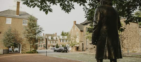 The back of a historic statue facing streets and buildings of Historic New Castle.