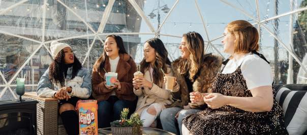 The image is of 5 women sitting inside an igloo that you can see out of during the day.