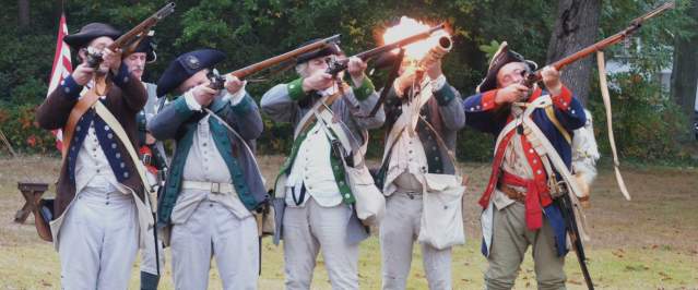 A group of historical Revolutionary War reenactors firing away at a Revolutionary War demonstration on Long Island.