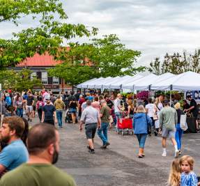 people walk the aisle between booths at a farmers market