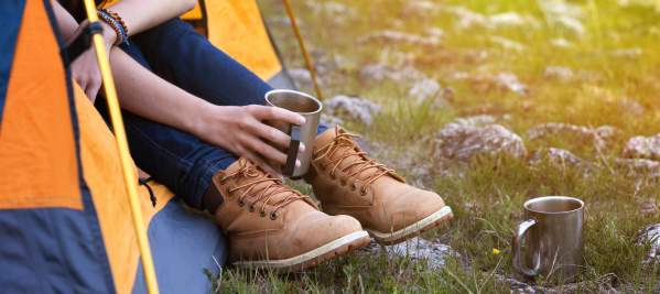 Someone sitting with their legs stuck outside of a tent while holding a coffee cup.