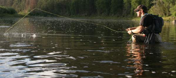 Man kneeling in a river while casting a fishing line.