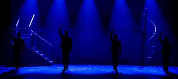 Sillouettes of four performers onstage underneath blue spotlights.