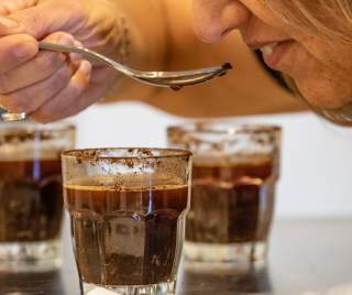 A close-up of someone raising a spoon from one of three coffee drinks in glass cups to their lips
