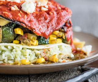 a colorful stack of different types of ingredients stacked between corn tortillas sit on a plate, next to silverware on a wooden table