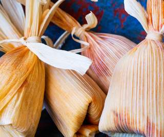Corn husk wrapped New Mexican Tamales sitting on a colorful tablecloth