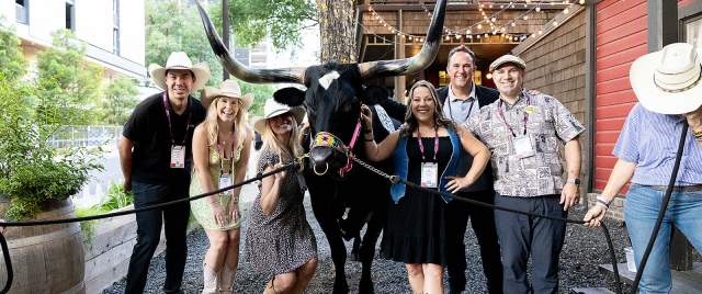 Group of people wearing cowboy hats and smiling at the camera while standing with a Longhorn.