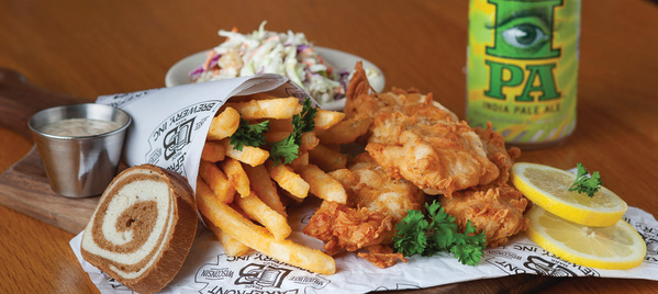 A painted figure sitting on a crescent moon hangs from the arched brick ceiling inside the Miller Caves.
A fish fry with fried cod, fries, coleslaw, rye bread, lemon slices and a can of IPA served on a wooden board.