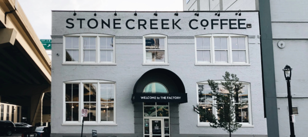 Exterior of Stone Creek Coffee’s white brick building with large front windows, black awning, and outdoor seating along the sidewalk.