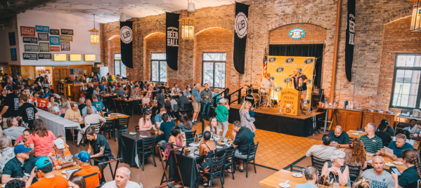 An open banquet hall filled with people eating food and drinking beer while a performer plays the accordion in the background.