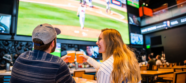 couple cheersing beer at bar with baseball on tv