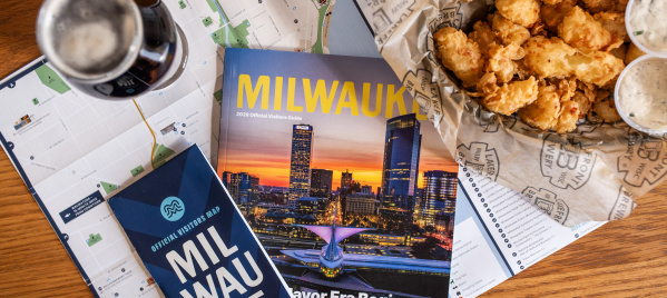 The 2026 Milwaukee Official Visitors Guide and Official Visitors Map are displayed with a beer and cheese curds on a table.
