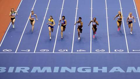 Eight runners race towards the camera on a blue running track with the Word BIRMINGHAM in bold letters at the end
