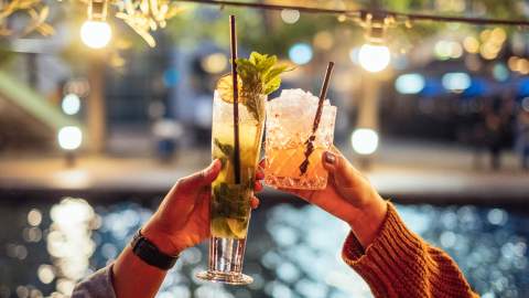 Two people raising cocktails in the air to cheers
