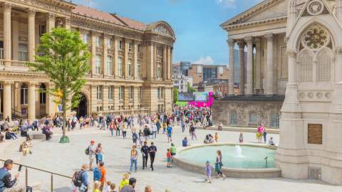Groups of people sitting outside in summer clothes. Surrounded by Chamberlain Square fountain and Birmingham Museum and Art Gallery