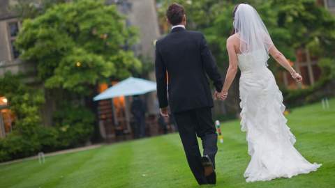 A bride and groom walk across the croquet lawn at The Greenway Hotel & Spa