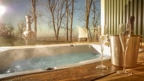 Hot tub bath at the Hilly Huts on FArncombe Estate. Steam rising from tub with bottle of sparkling wine, glasses and chimnea in background