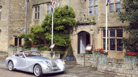 A vintage car parked in front of the Cotswold stone entrance to The Lygon Arms Hotel in the Cotswolds