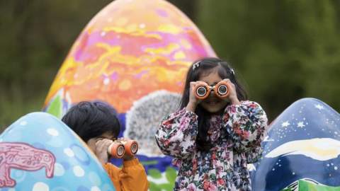 children in puddlesuits looking through binoculars, huge easter eggs in the background