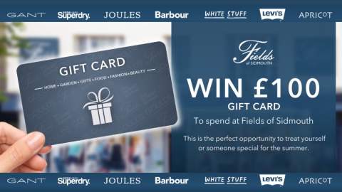 A hand holds a Fields gift card against a blurred background. Text reads: "Win £100 gift card to spend at Fields of Sidmouth." Logos of brands are above.